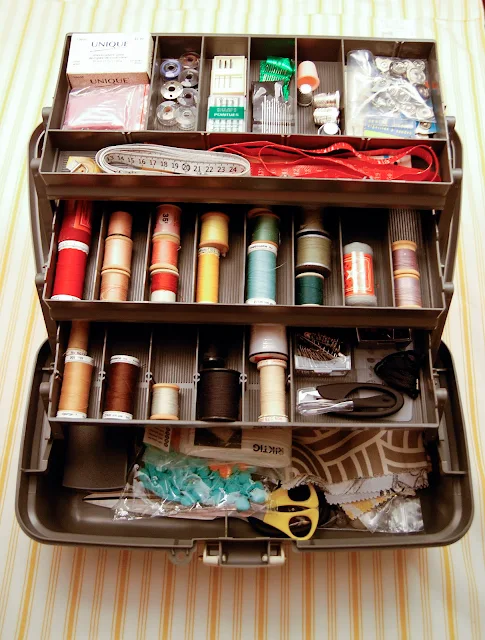 A three-tier, study plastic sewing toolkit with sewing supplies neatly stored in its various compartments.